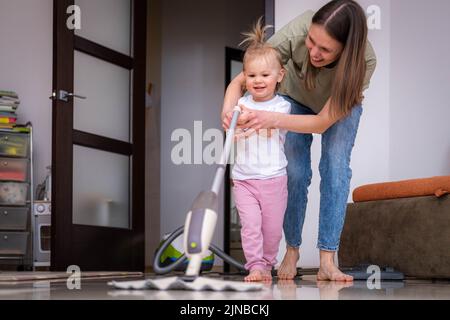 Piccola figlia pulizia in casa, bambino spolverare, carino piccola helper ragazza lavaggio pavimento con mop, la famiglia felice pulisce la camera, Foto Stock