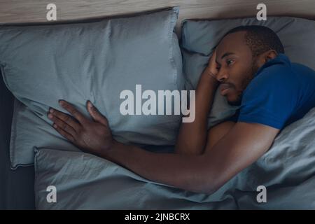 Unhappy Black Man toccare il cuscino sdraiato in Letto interno Foto Stock