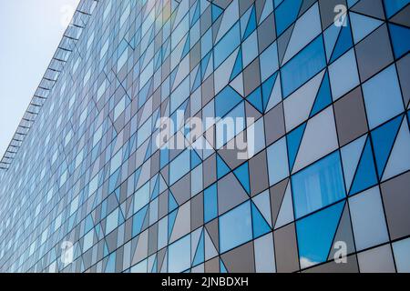 Un primo piano di facciata grigia sfaccettata di un edificio moderno con un cielo blu chiaro Foto Stock