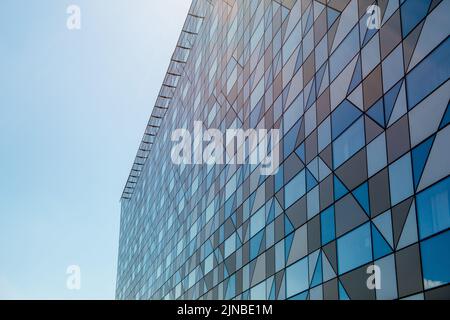 Un primo piano di facciata grigia sfaccettata di un edificio moderno con un cielo blu chiaro Foto Stock