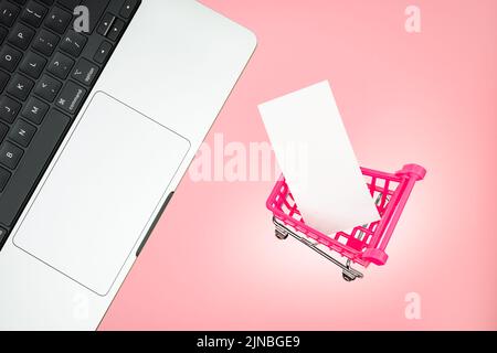 Carrello per laptop con etichetta di carta bianca carta bianca su sfondo rosa. Concetto di shopping rosa per laptop. Vendita carrello laptop tastiera online Foto Stock