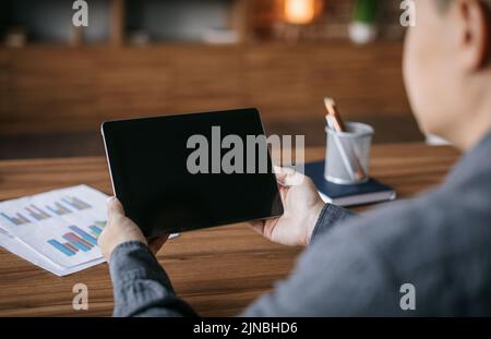 Un uomo giapponese adulto ha una videochiamata sul tablet con schermo vuoto al tavolo all'interno dell'ufficio, sul retro Foto Stock