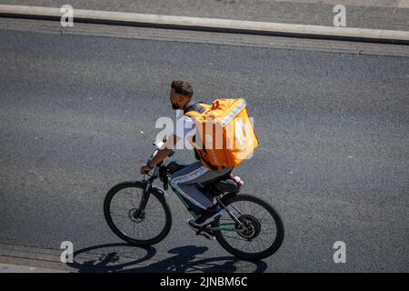 Consegna a domicilio. Mangi il pilota di consegna della bici con il grande zaino arancione, i cicli lungo una strada in Inghilterra. Ripresa dall'alto Foto Stock