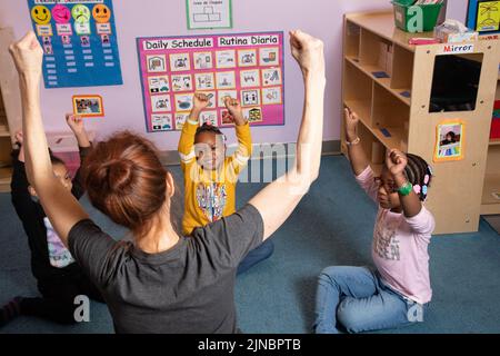 Istruzione Preschool cura dei bambini dai 4 anni in su insegnante di yoga che lavora con un piccolo gruppo di ragazze Foto Stock