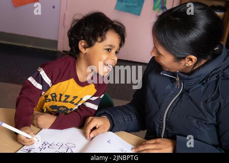 Istruzione Preschool bambino cura 4 anni ragazzo con madre all'inizio del giorno scrivere numeri nel suo libro di segno-in Foto Stock