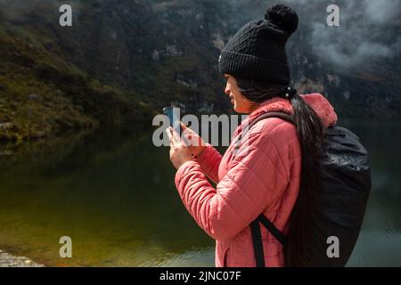Una donna che si trova contro un flusso e scatta foto con il suo telefono Foto Stock