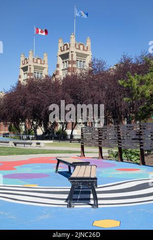 Panchine presso il campus SAIT (Southern Alberta Institute of Technology) con bandiere canadesi e Albertan che volano sull'Heritage Hall di Calgary, Canada Foto Stock