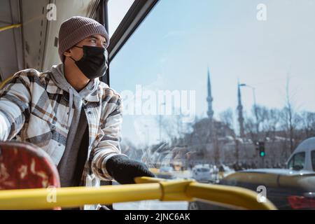 uomo asiatico con maschera che guarda attraverso la finestra di un autobus Foto Stock