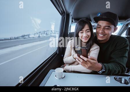 coppia asiatica che usa lo smartphone insieme mentre viaggia in auto Foto Stock