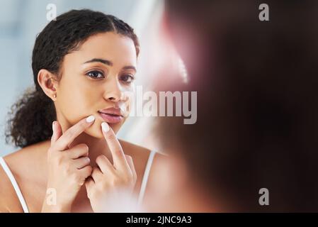 Schiacciare potrebbe lasciare segni permanenti. Una bella giovane donna schiacciare un pimple nello specchio. Foto Stock