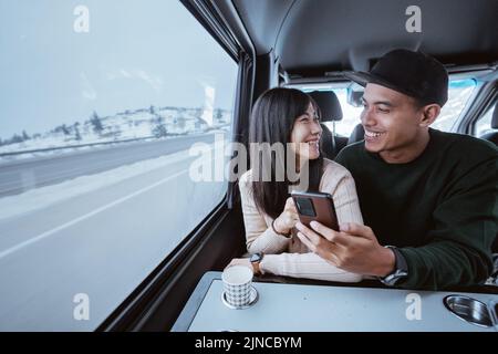 coppia asiatica che usa lo smartphone insieme mentre viaggia in auto Foto Stock