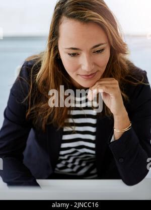 Questo sembra piuttosto interessante. Scatto ad angolo alto di una donna d'affari attraente che lavora su un computer nel suo ufficio. Foto Stock