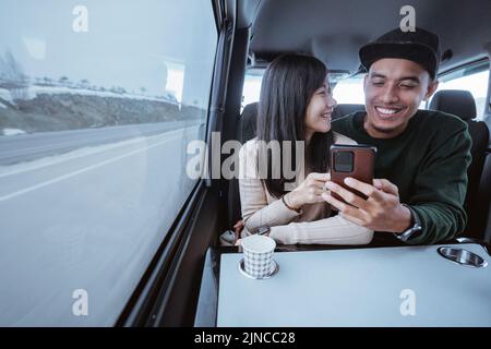 coppia asiatica che usa lo smartphone insieme mentre viaggia in auto Foto Stock