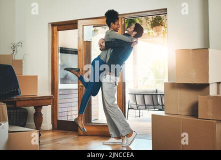 Coppia interrazziale gioiosa che si sposta in una nuova casa insieme abbracciando sentirsi felice ed eccitato. Amanti diversi, amorevoli e giovani che si trasferiscono in una casa Foto Stock