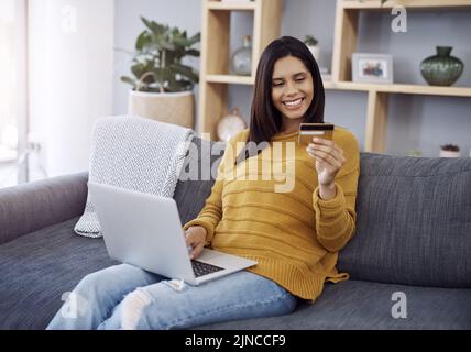 Fare shopping nel comfort di casa propria. Una giovane donna attraente che fa shopping online sul suo laptop mentre si rilassa su un divano a casa. Foto Stock