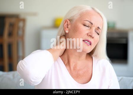 Donna matura che soffre di dolore al collo in cucina, primo piano Foto Stock