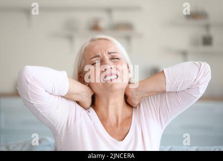 Donna matura che soffre di dolore al collo in cucina, primo piano Foto Stock