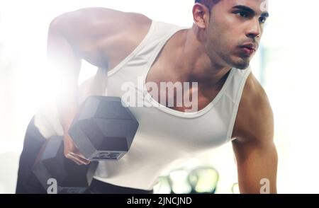 I muscoli li usano o li perdono. Un bel giovane sportivo che si allena con i manubri in palestra. Foto Stock