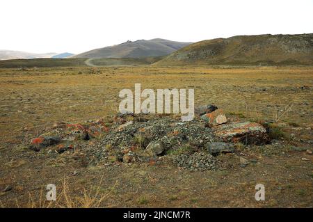 Un piccolo tumulo di pietra saccheggiato da antichi marinai in una valle autunnale ai piedi di una catena montuosa. Chui steppe, Altai, Siberia, Russia. Foto Stock