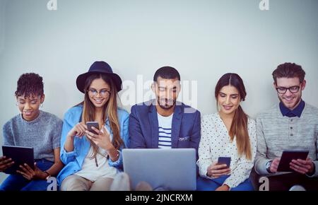 Collegati online e non avrai mai bisogno di pile di documenti cartacei. Studio di un gruppo di giovani uomini d'affari che utilizzano la tecnologia wireless mentre sono in fila Foto Stock