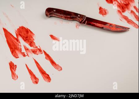 La lama sanguinante e la mano stampano nel sangue su un tavolo bianco. Foto Stock