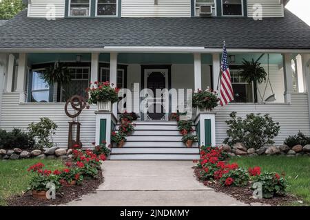 Bella casa bianca con un portico anteriore e marciapiede decorato con gerani rossi reminiscenza del Grand Hotel sull'isola di Mackinac, Michigan. Foto Stock