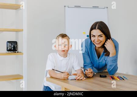 Lezione privata. Una giovane insegnante attenta tutor che aiuta la pupilla del ragazzino con lo studio, errori corretti spiegano il materiale di apprendimento. Madre sorridente Foto Stock