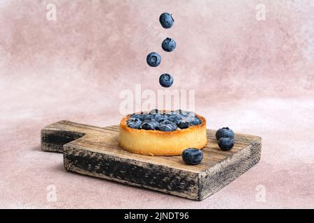 Design surreale con bacche galleggianti. Torta di mirtilli su un asse di legno. Crostata di mirtillo. Concetto creativo del cibo del mosca. Foto Stock