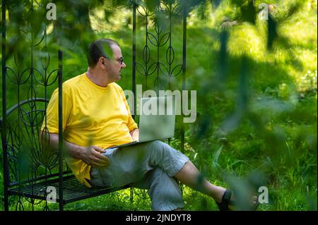uomo di mezza età con laptop che lavora all'esterno in giardino, concetto di casa verde ufficio Foto Stock
