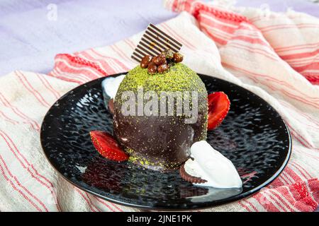 Torta dolce singola. Torta al cioccolato smaltata, un pezzo, su piatto nero con torta al pistacchio. Viene servito su un piatto con gelato e fragole. Foto Stock