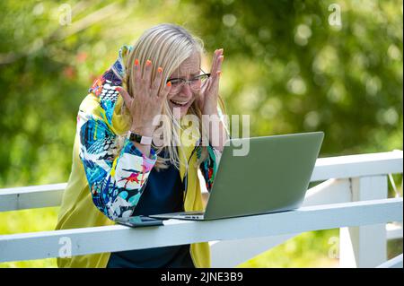 donna emotiva senior con laptop che effettua videochiamate e gesturing attivo, comunicazione online Foto Stock