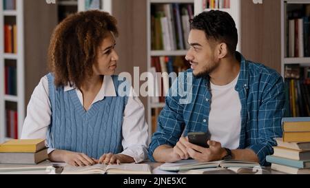 Gli studenti fanno i compiti in biblioteca lavoro di squadra lavorando sul progetto congiunto cute ragazza spiegare compito a maschio amico scrivere note preparazione per esame comunicare Foto Stock