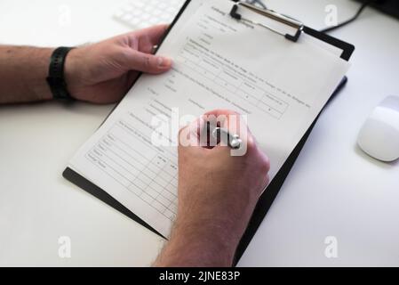 primo piano della persona che compila il modulo o il sondaggio presso la scrivania dell'ufficio Foto Stock