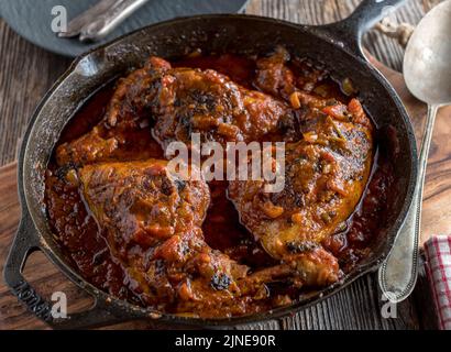 Cosce di pollo brasate con salsa di pomodoro italiana in una rustica padella di ghisa su un tavolo di legno Foto Stock