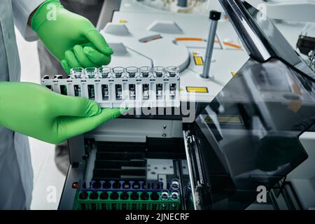 Il tecnico di laboratorio scarica i campioni di analisi del sangue nell'analizzatore automatico biochimico del sangue per la biochimica nel moderno laboratorio medico Foto Stock