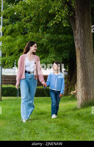 felice donna e ragazza tenendo le mani e guardarsi l'un l'altro mentre camminano nel parco, immagine di riserva Foto Stock