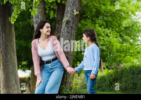 giovane donna e bambino tenendo le mani e guardando gli altri vicino agli alberi nel parco, immagine stock Foto Stock