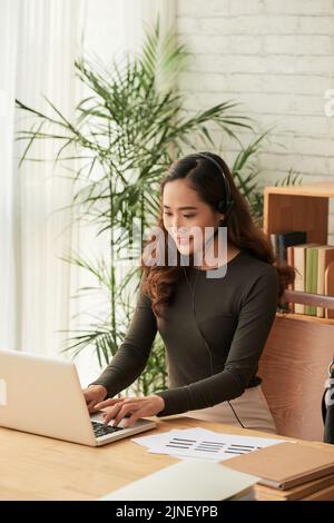 Ragazza allegra e graziosa in cuffia che lavora al computer Foto Stock