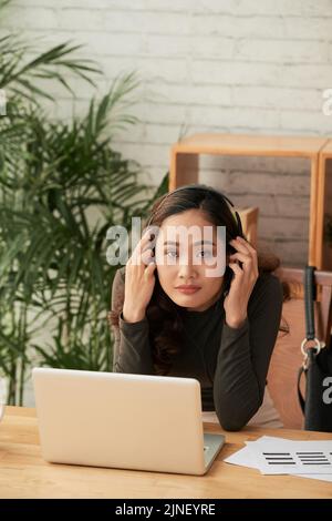 Bella donna vietnamita che indossa le cuffie prima di lavorare sul notebook Foto Stock