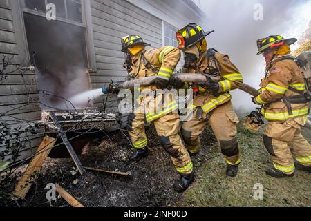 Un team di tre persone utilizza un tubo flessibile per spruzzare acqua attraverso una finestra per cercare di spegnere l'incendio al suo interno come il Dipartimento dei vigili del fuoco di Bridgehampton, con m Foto Stock