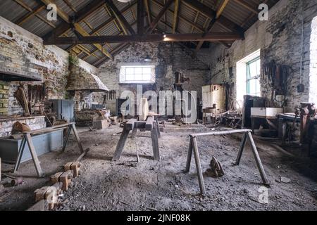 Una gigantesca ruota affilatrice in pietra al centro del vecchio e sporco negozio di fabbro. Al Big Pit National Coal Museum di Pontypool, Galles, United Kingdo Foto Stock