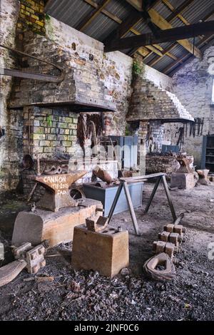 Un'incudine arrugginita nel mezzo dell'area sporca e vecchia del negozio di fabbro. Al Big Pit National Coal Museum di Pontypool, Galles, Regno Unito. Foto Stock