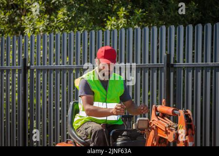 Un uomo su un miniescavatore livella un pezzo di terra, allenta il terreno Foto Stock