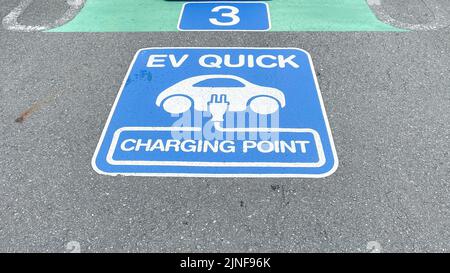 Un cartello per un caricabatterie rapido EV sul pavimento di un parcheggio sul tetto presso un centro commerciale EON, blu e bianco, con una spina e un'auto Foto Stock