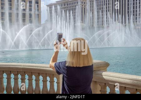 Una donna che scatta foto verticali con un telefono cellulare delle fontane d'acqua a Bellagio Las Vegas Foto Stock