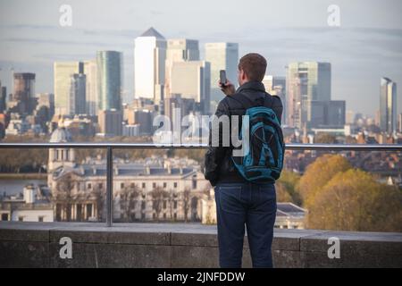 Londra, Regno Unito - 3 novembre 2021 - Vista posteriore di un turista maschile che scatta foto del paesaggio urbano londinese dalla collina di Greenwich Foto Stock