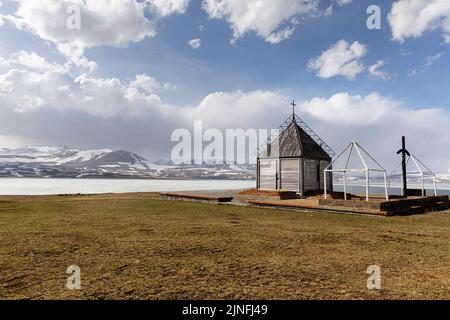 Piccola chiesa presso il bellissimo e ghiacciato lago Paravani in primavera, Javakheti Volcanic Plateau, Georgia Foto Stock