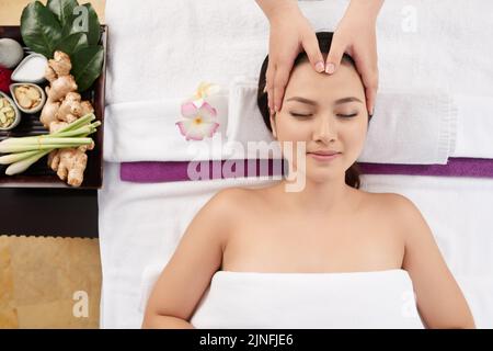 Therapeust massaggiare la testa e il viso della cliente femminile, vista dall'alto Foto Stock