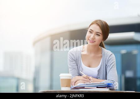 Bella signora vietnamita di affari pensiva scrivere idee per il suo progetto Foto Stock