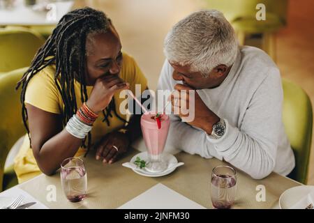 Coppia matura che condivide un delizioso frullato di fragole in un bar. Coppia senior spensierata che si trova in un ristorante. Felice coppia matura godere Foto Stock